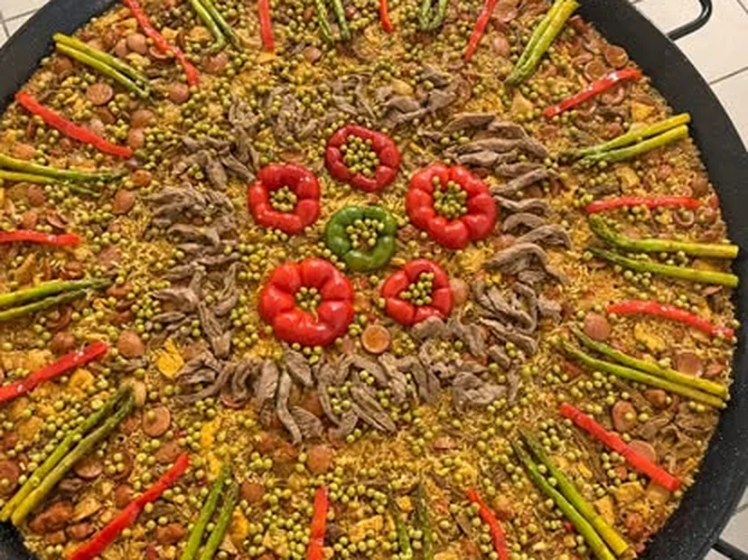 Paella de carnes terminada en una paellera grande, montada en círculo con pimientos y espárragos